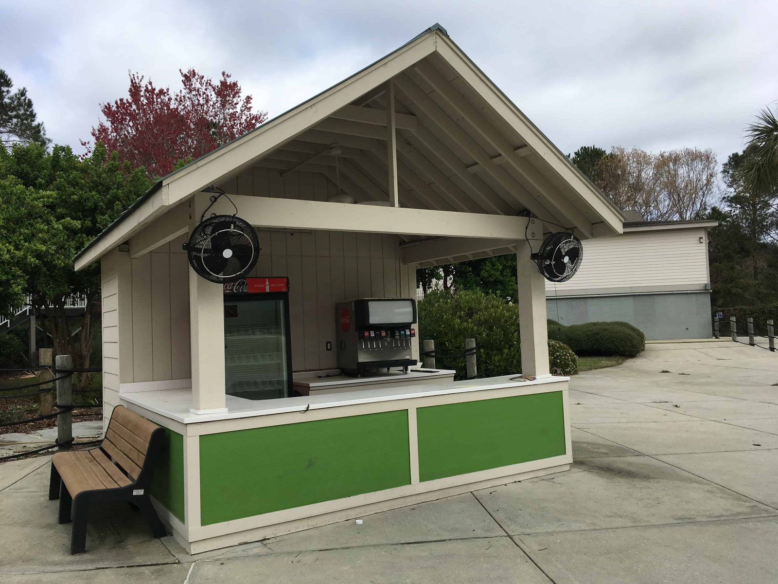Outdoor kiosk with a bench, vending machines, and speakers on a cloudy day.