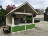 Outdoor kiosk with a bench, vending machines, and speakers on a cloudy day.
