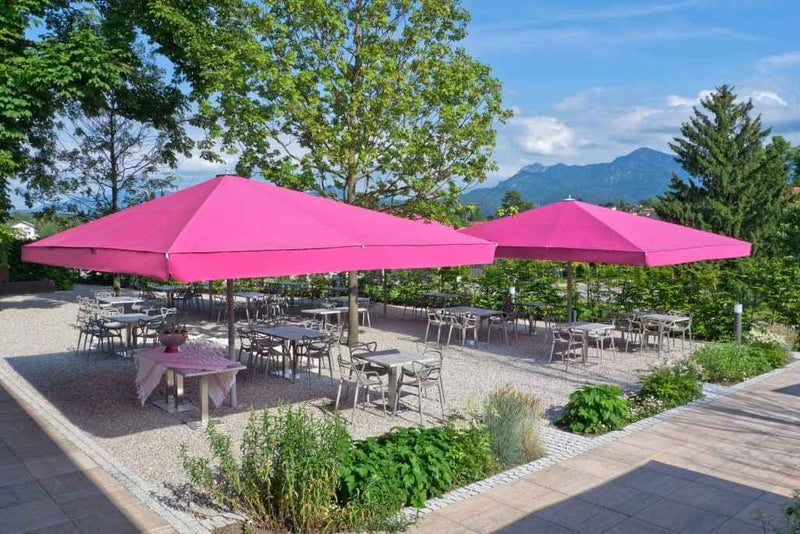 Outdoor setting with pink umbrellas over tables, surrounded by greenery and mountains.