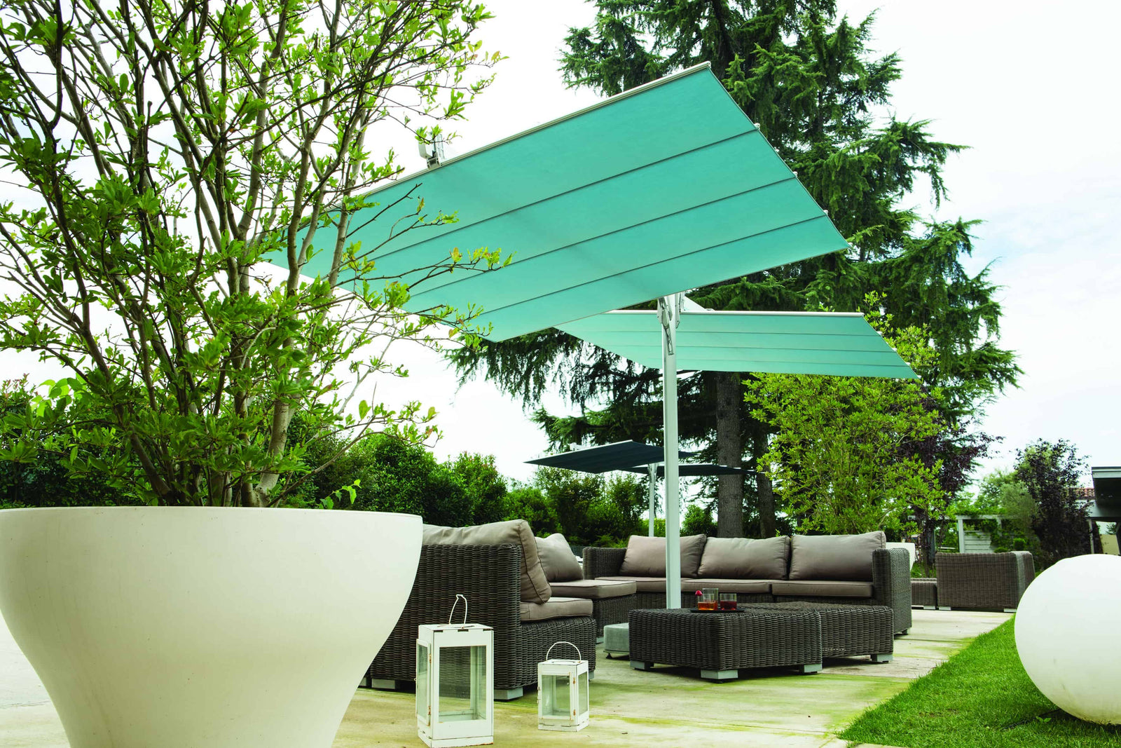 Outdoor patio with green umbrella, gray sofa, and white table in a garden setting.