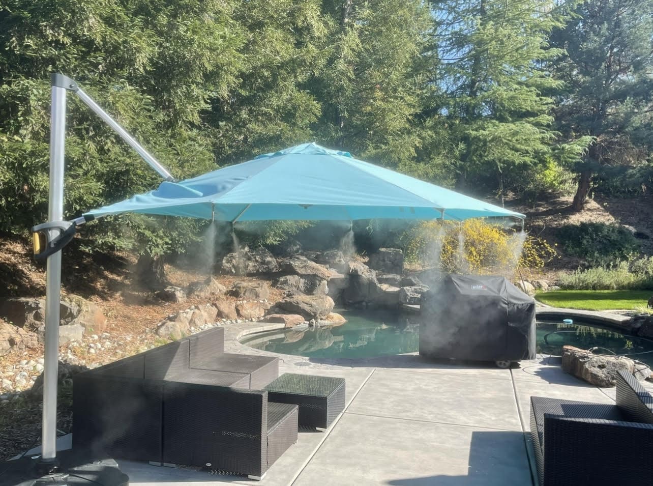 Outdoor patio with a blue umbrella, chairs, and a pool area surrounded by trees.