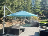 Outdoor patio with a blue umbrella, chairs, and a pool area surrounded by trees.