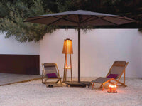 Outdoor setting with two lounge chairs under a large umbrella, illuminated by a floor lamp and candles.