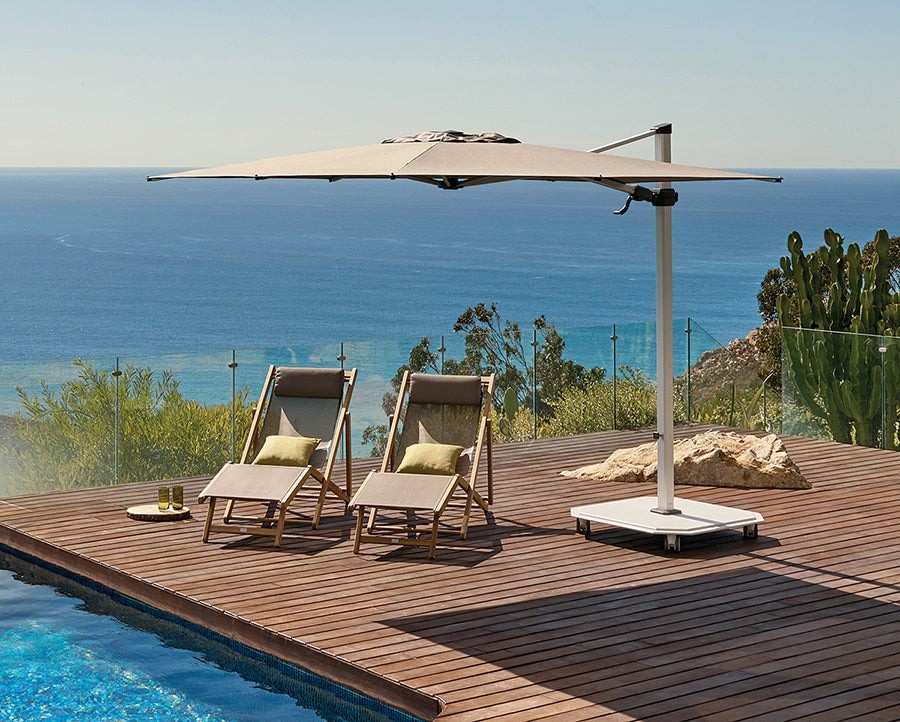 Outdoor setting with lounge chairs, table, and umbrella on a wooden deck by a pool with ocean view.