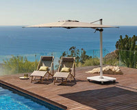 Outdoor setting with lounge chairs, table, and umbrella on a wooden deck by a pool with ocean view.