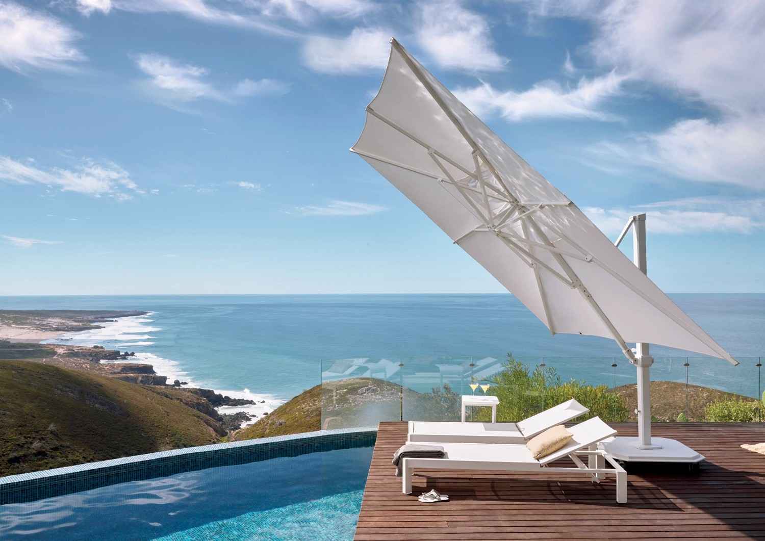 White umbrella and lounge chairs by a pool with ocean view