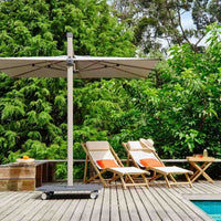 Outdoor setting with lounge chairs, umbrella, and table on a wooden deck surrounded by greenery.