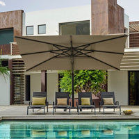 Large patio umbrella over four chairs by a poolside in front of a modern building.