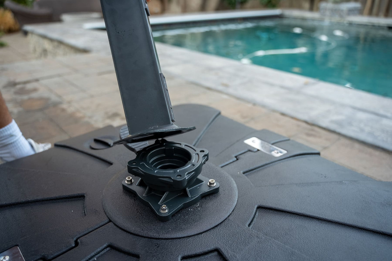Close-up of a black umbrella base with a pool in the background