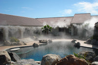 Outdoor pool area with mist rising from the water, surrounded by rocks and a building.
