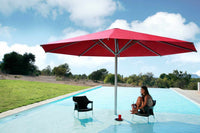 Person sitting under a large red umbrella by a pool with a scenic background