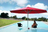 Person sitting under a large red umbrella by a pool with a scenic background