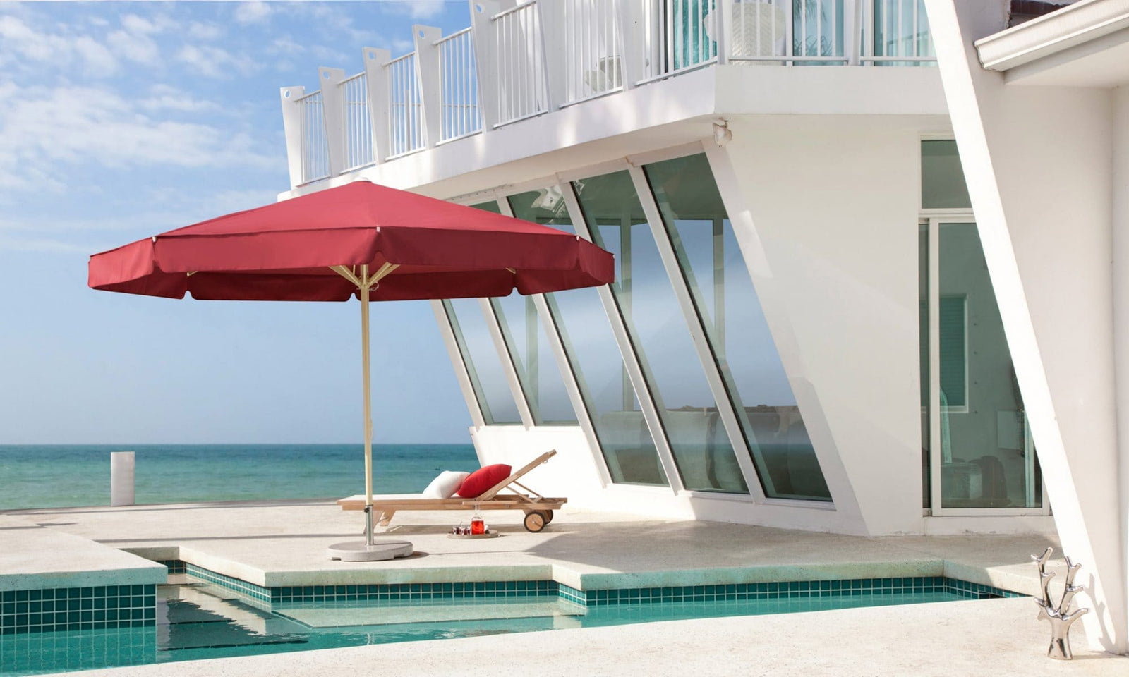 Red umbrella and lounge chair by a pool with ocean view