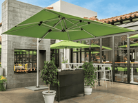 Green outdoor umbrella in an urban setting with a building and patio in the background.