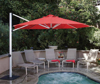 Red patio umbrella over a seating area by a pool with chairs and a small table.