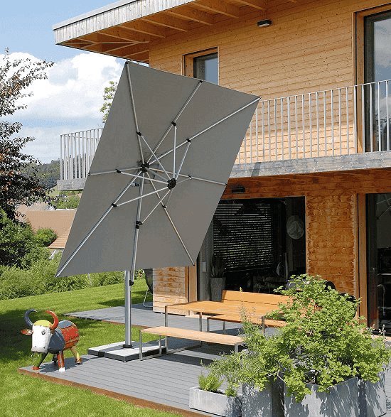 Large gray patio umbrella in front of a modern wooden house with a garden.