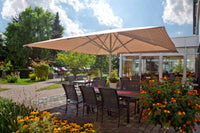 Outdoor dining area with large umbrella, tables, chairs, and flowers on a sunny day.
