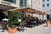 Outdoor seating area with tables, chairs, and large umbrellas in front of a building with 'Sternbräu' signage.