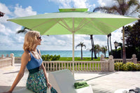 Woman sitting under a large green patio umbrella with a scenic ocean view in the background.